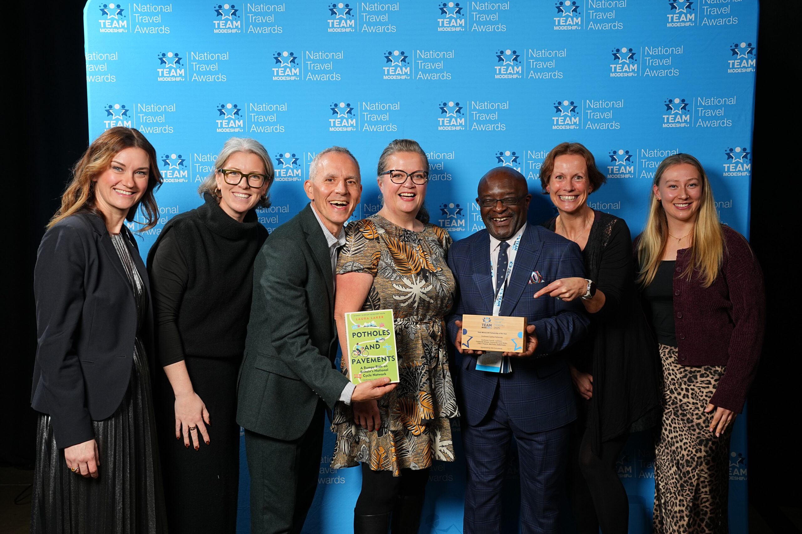 Team Modeshift Partnership of the Year Sponsored by SAJ Consultants Southwark Cycling Partnership Southwark Council, JoyRiders, Peddle My Wheels, Community Cycle Works, PWLC Projects, Met Police, BetterPoints Group of people stand smiling, central figures holding their TeamModeshift Award