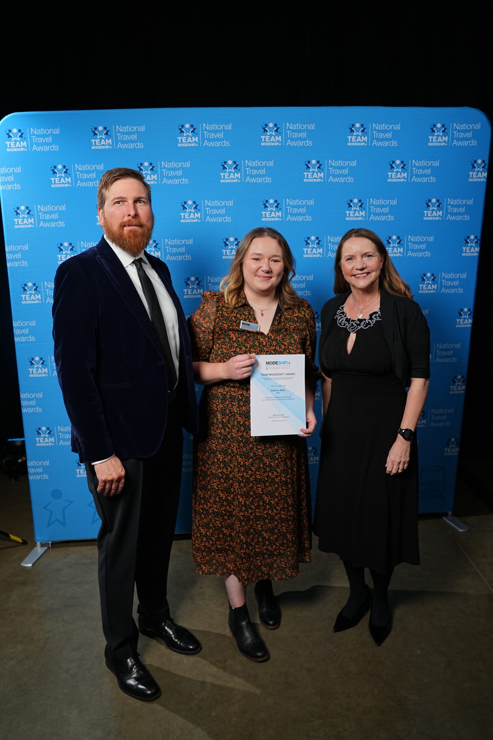 Saffron Allen, TPS poses with Honorary Member Certificate, two people smile at camera either side.