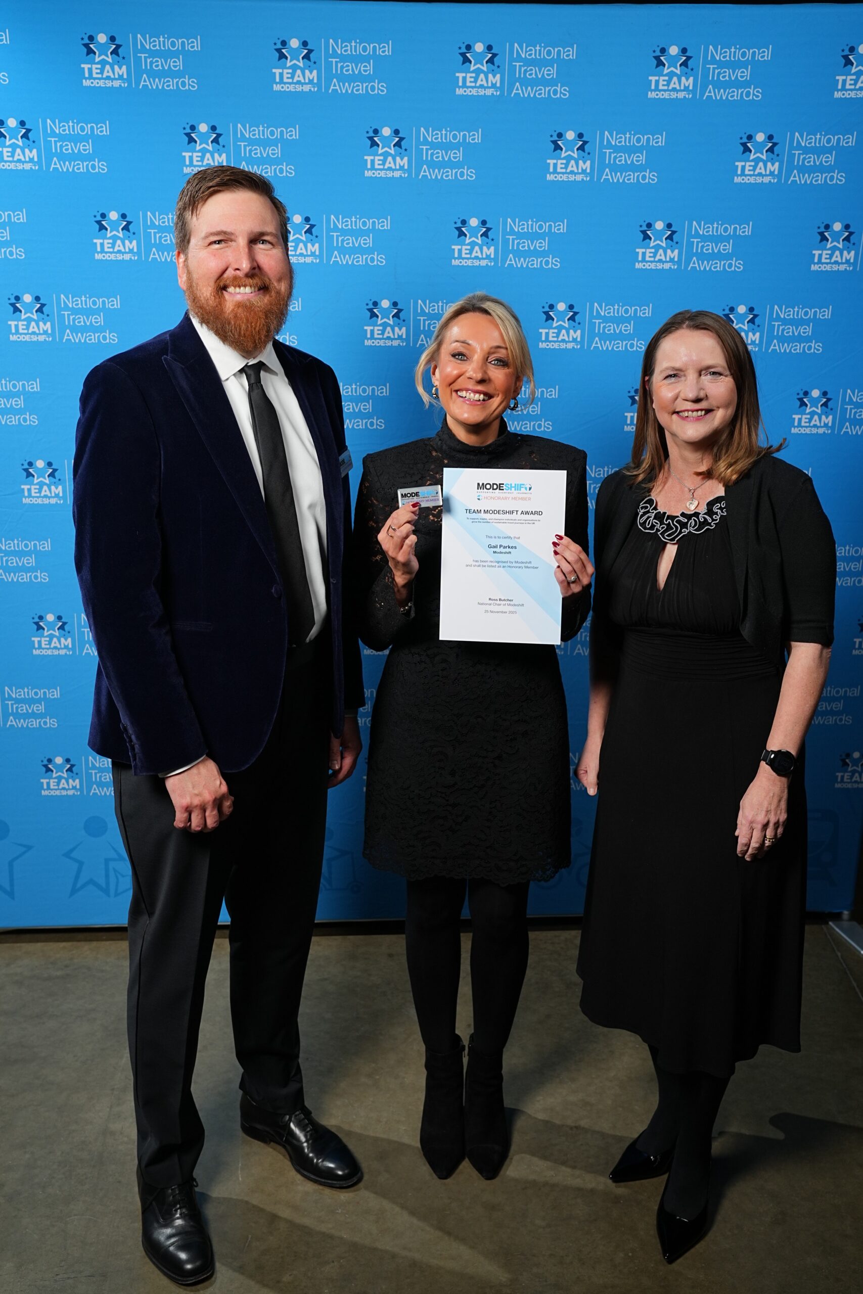 Gail Parkes, Modeshift poses with Honorary Member Certificate, two people smile at camera either side.