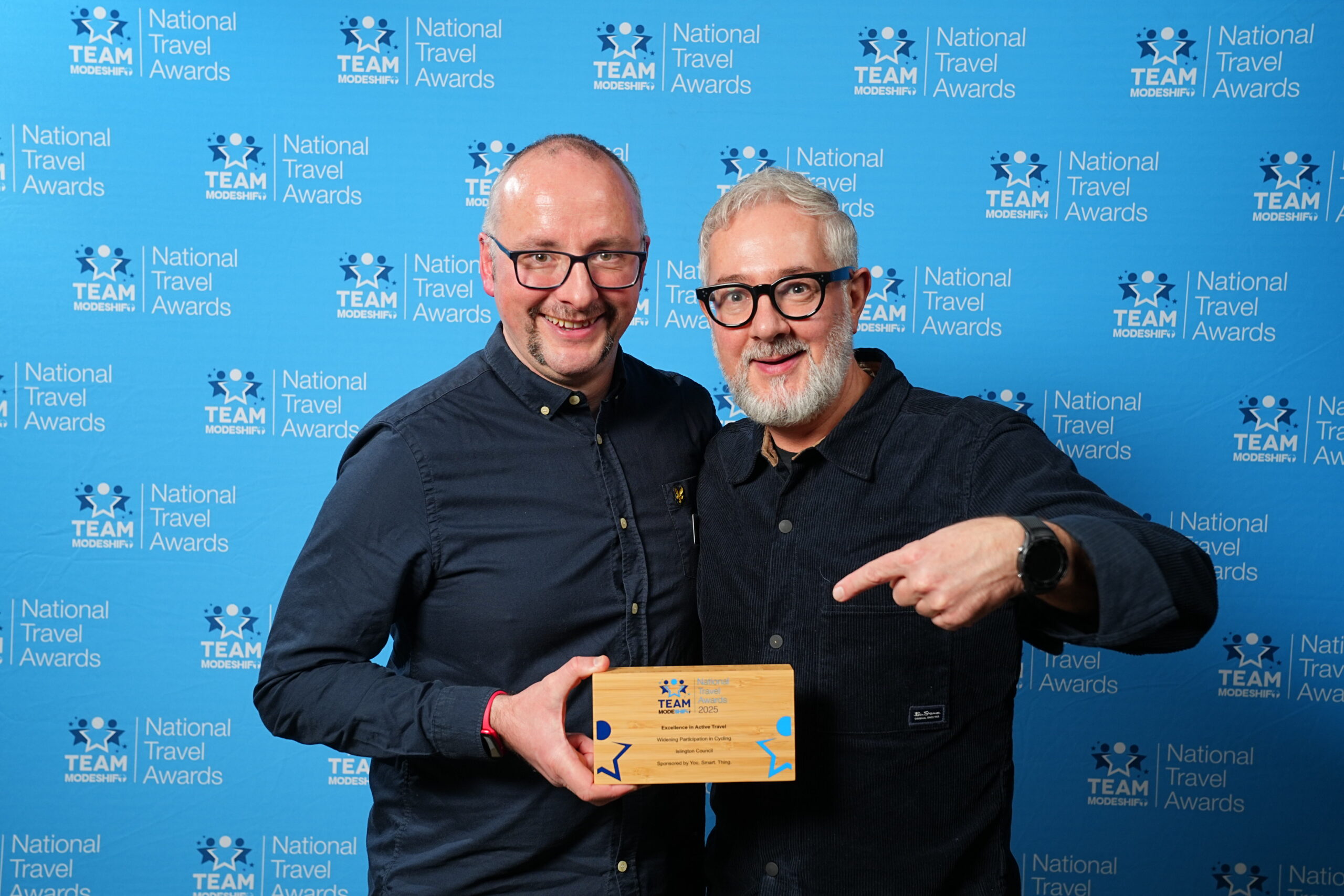 YST CEO Chris Thompson collects the ‘Excellence in Active Travel’ award on behalf of Islington Council. Two men pose holding trophy in front of Modeshift branded background.
