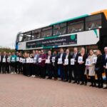 Group of people standing in front of a double-decker bus holding signs that spell 'Preparing for Success'.