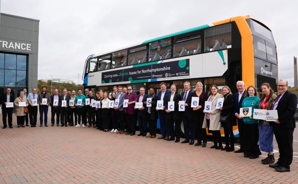 Group of people standing in front of a double-decker bus holding signs that spell 'Preparing for Success'.