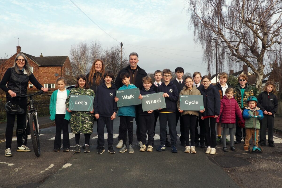 Group of children and adults standing outdoors holding signs that say 'Let's Walk Wheel Cycle' promoting active travel.