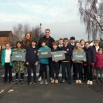 Group of children and adults standing outdoors holding signs that say 'Let's Walk Wheel Cycle' promoting active travel.
