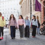 A group of women walks down a city street on a sunny day.