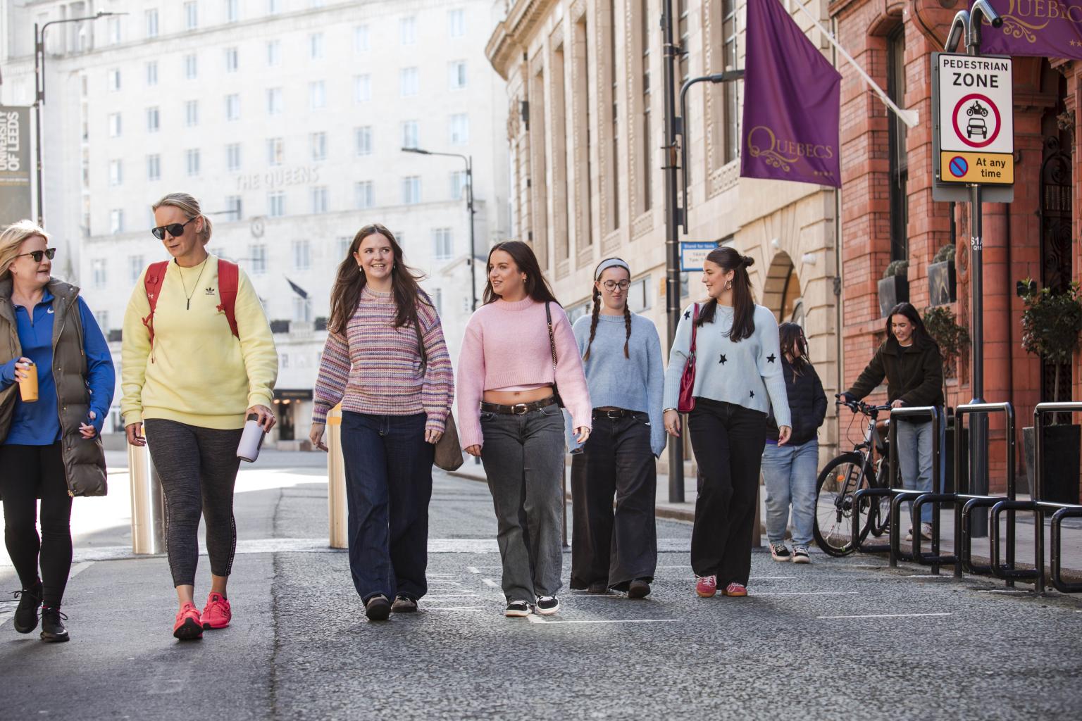 A group of women walks down a city street on a sunny day.