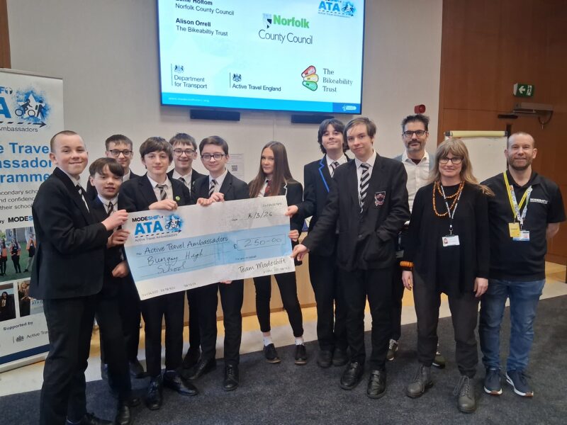 Group of students in uniform hold a large novelty check for £250.00 payable to Bungay High School, with adults standing behind them.