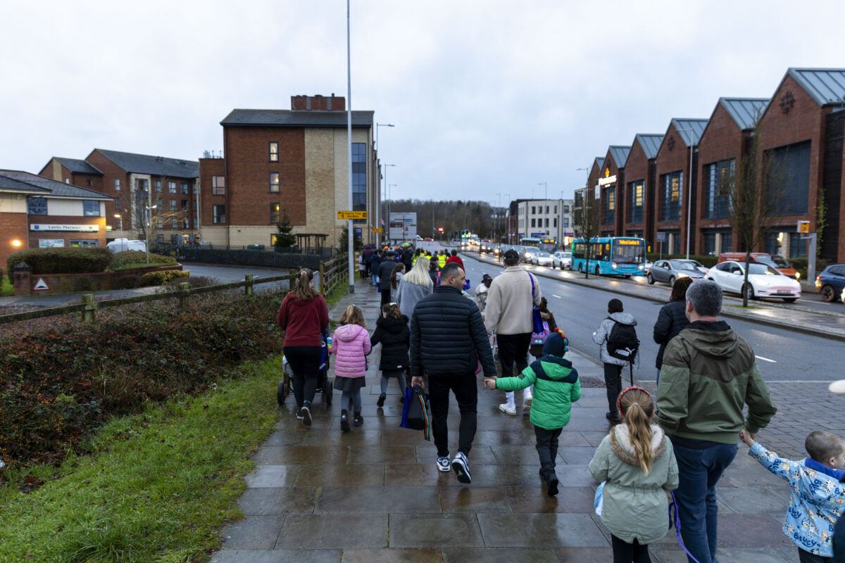 A group of people, including adults and children, walk along a wet sidewalk next to a street with traffic and businesses. Telford and Wrekin – Celebrating their first STARS accredited school.