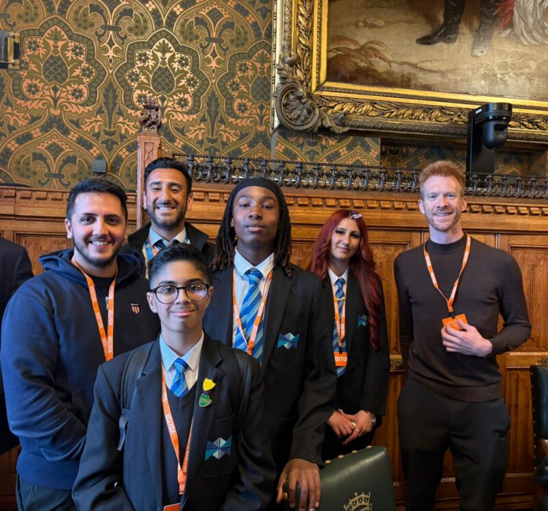 A group of students in school uniforms and adults pose for a photo in a room with ornate patterned wallpaper and a large framed painting.
