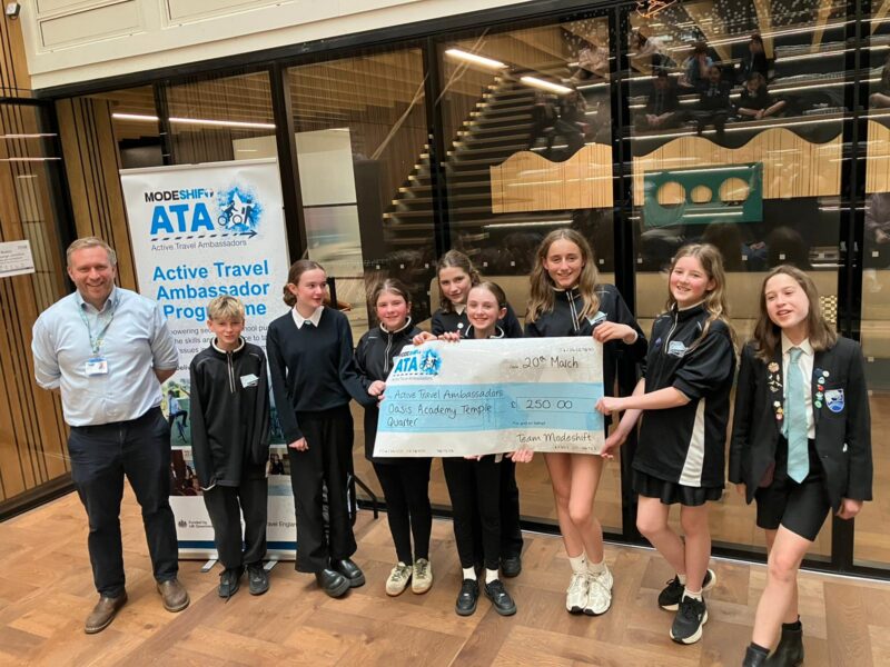 Students in school uniform pose with a large cheque for the Active Travel Ambassadors Campaign funding awarded at the Campaign Junction event.