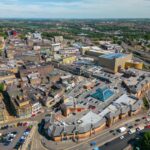 BetterPoints launches physical activity rewards programme across Barnsley. Aerial view of a bustling town center with a large shopping complex surrounded by streets and parked cars under a partly cloudy sky.