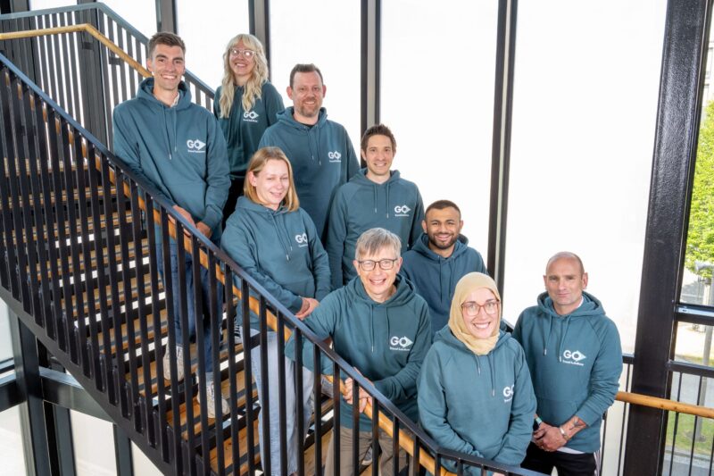 group of adults wearing blue hoodies stood on stairs smiling 
