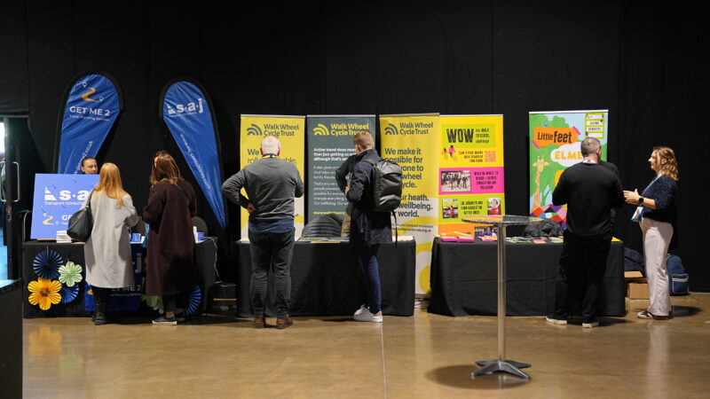 People stand at exhibition booths with banners promoting cycling, transport, and children's programs.