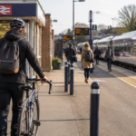 A person wearing a cycling helmet and backpack walks with a bicycle along a train platform next to a stationary train.