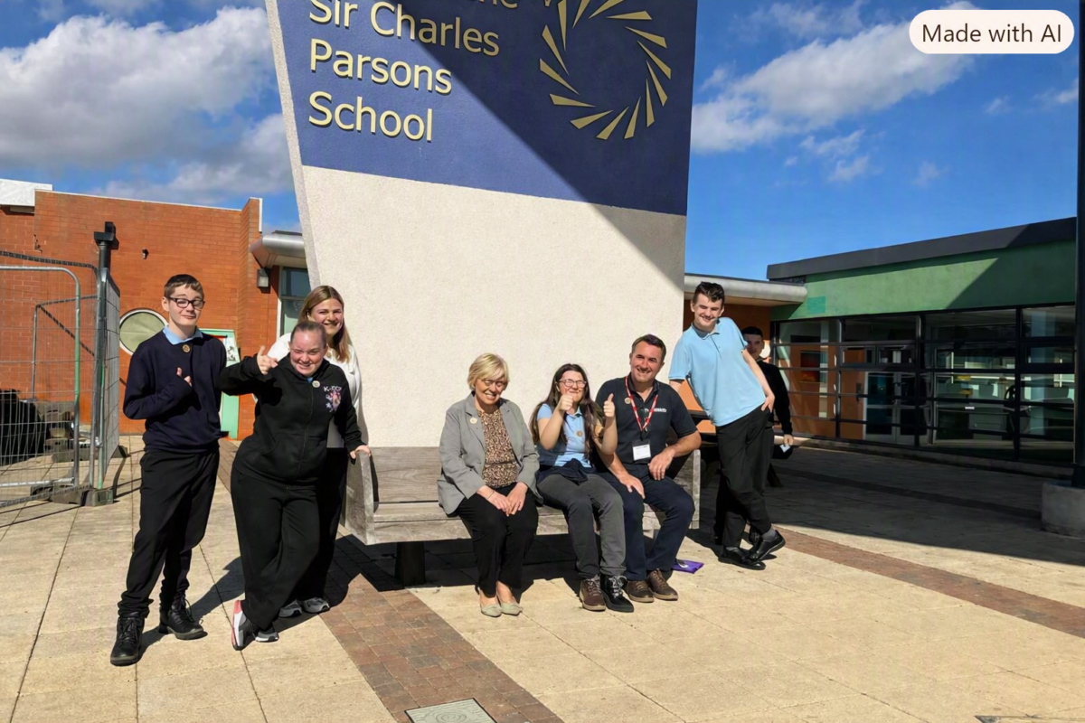 A group of people, including students and adults, are gathered outdoors in front of a sign that reads "Sir Charles Parsons School". Several individuals are smiling and giving thumbs up.